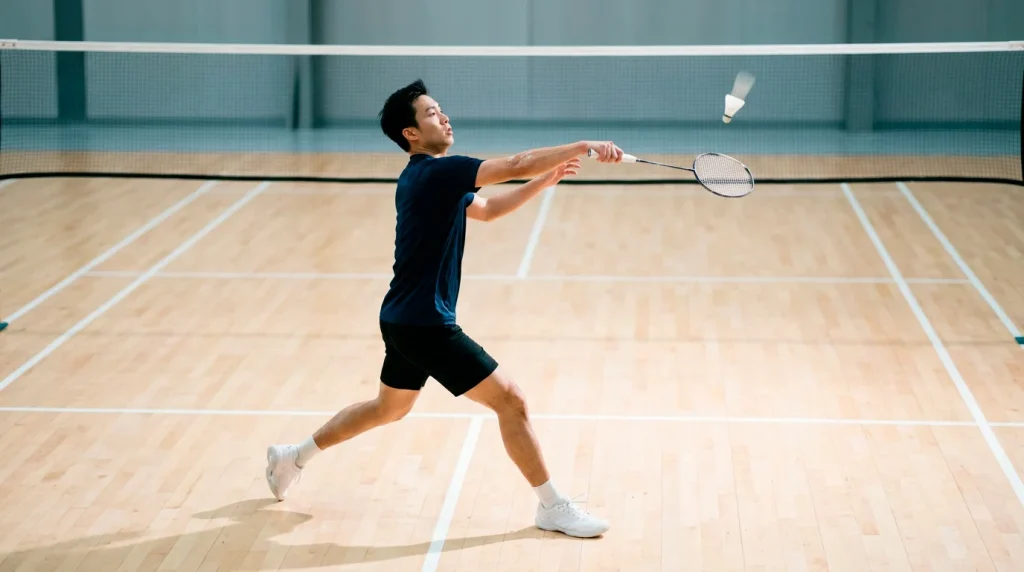 Badminton-Spieler im Smash auf einem Indoor-Hartholzcourt als Bildmotiv zu Badminton Wettarten